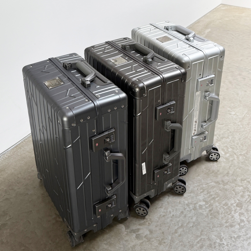 Two space grey GUNDEL suitcases with a line pattern standing in a field with dry grass.